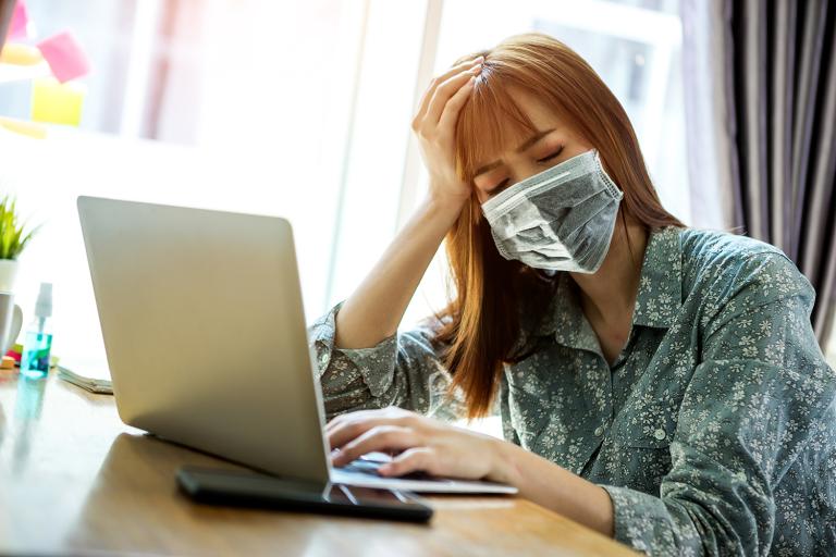 a fatigued woman in a mask working from home