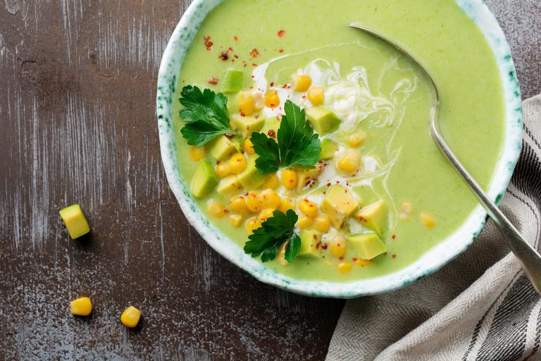 a bowl of creamy green soup with corn, diced avocado, and spices